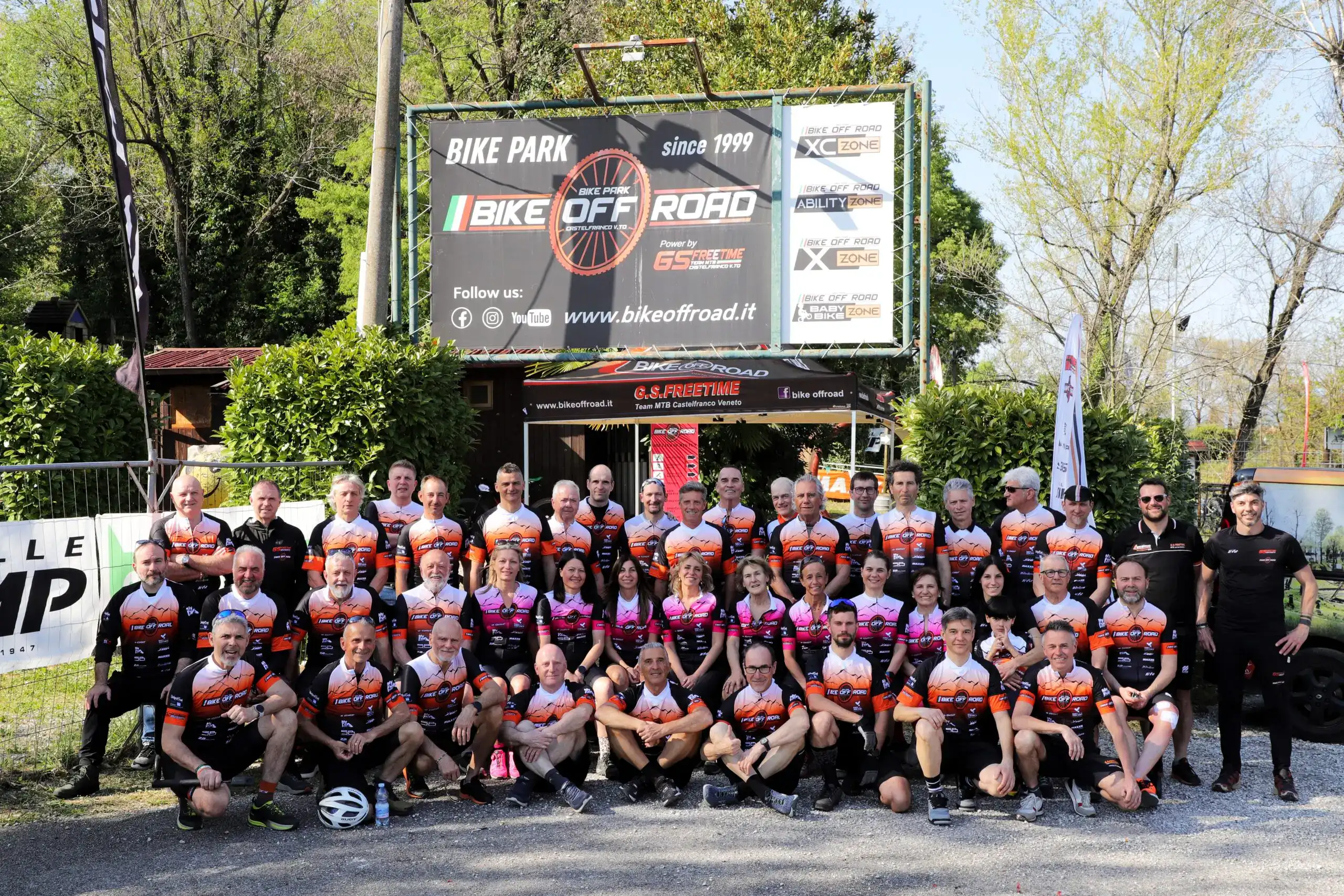 Gruppo di ciclisti in posa davanti a un cartellone pubblicitario di Bike Off Road.
